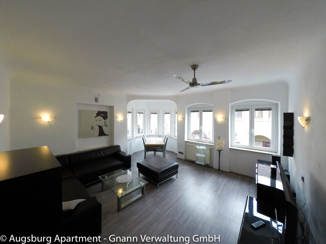 Wohnzimmer mit schwarzem Ledersofa, Glastisch und Fensterfront in einem Business Apartment in Augsburg