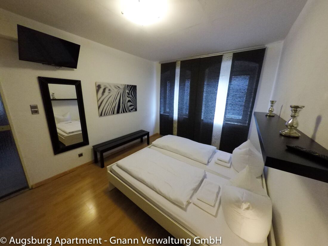 Schlafzimmer mit Doppelbett, Wandspiegel und TV in einem möblierten Apartment in Augsburg