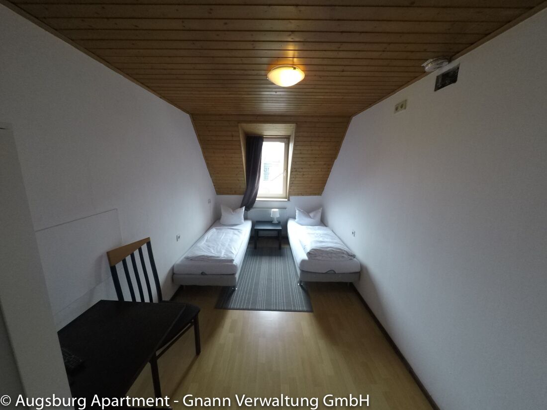 Zweibettzimmer mit Holzdecke, Stuhl und Fenster in einer Monteurwohnung in Augsburg